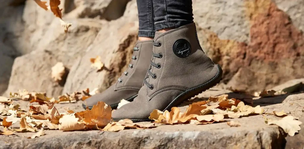 Eine junge Frau, die überzeugte Barfußschuh trägerin ist, steht bei herbstlichen Wetter auf ihren Zehenspitzen in den Leguano chester im Laub.
